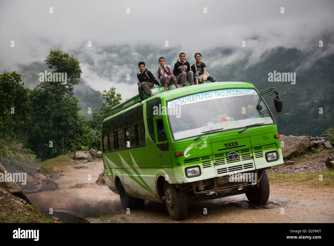 A bus makes it's way through the mountains in Dolakha district. The roads are rough and some passengers are on the rooftop. Stock Photo