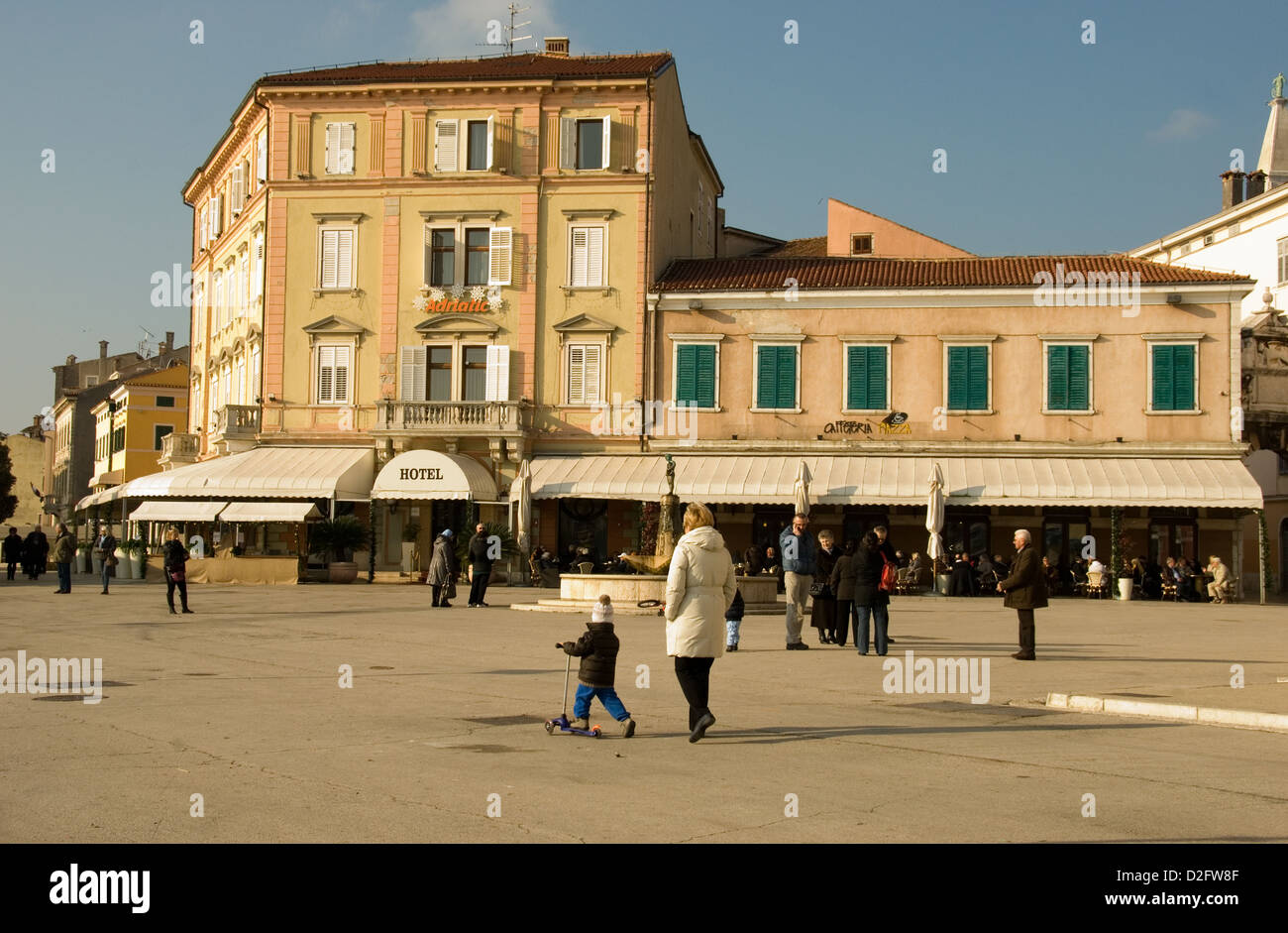 Rovinj town square at the Adriatic Hotel in the old town, pedestrian's walking and children playing in the warm winter climate. Stock Photo