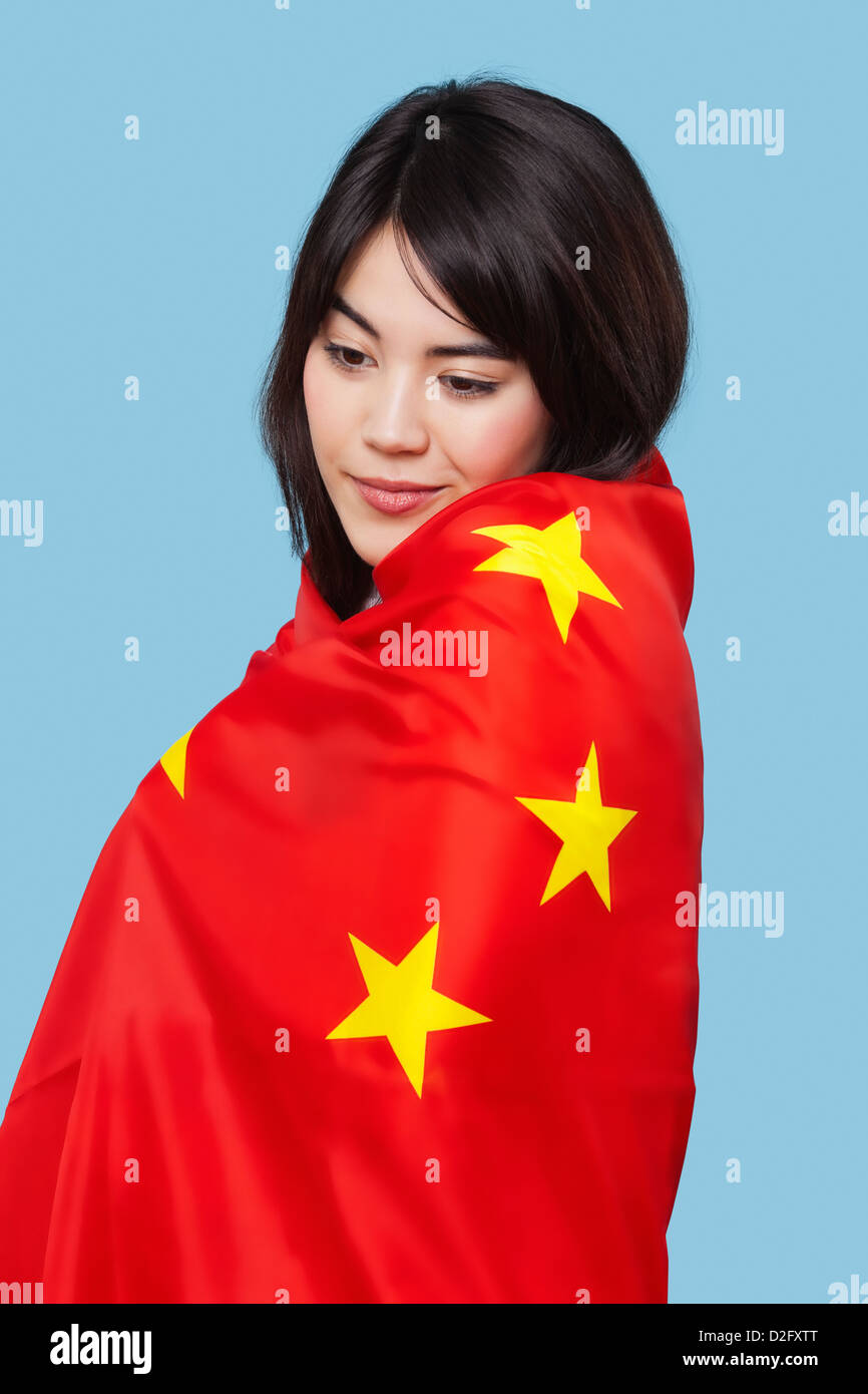 Patriotic young woman wrapped in Chinese flag over blue background