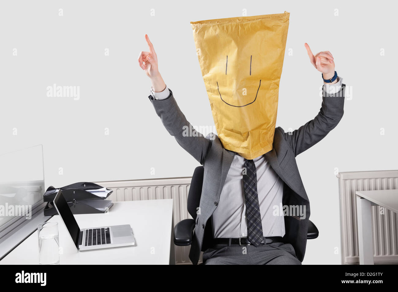 Businessman cheering with smiley drawn on paper bag over face in office Stock Photo