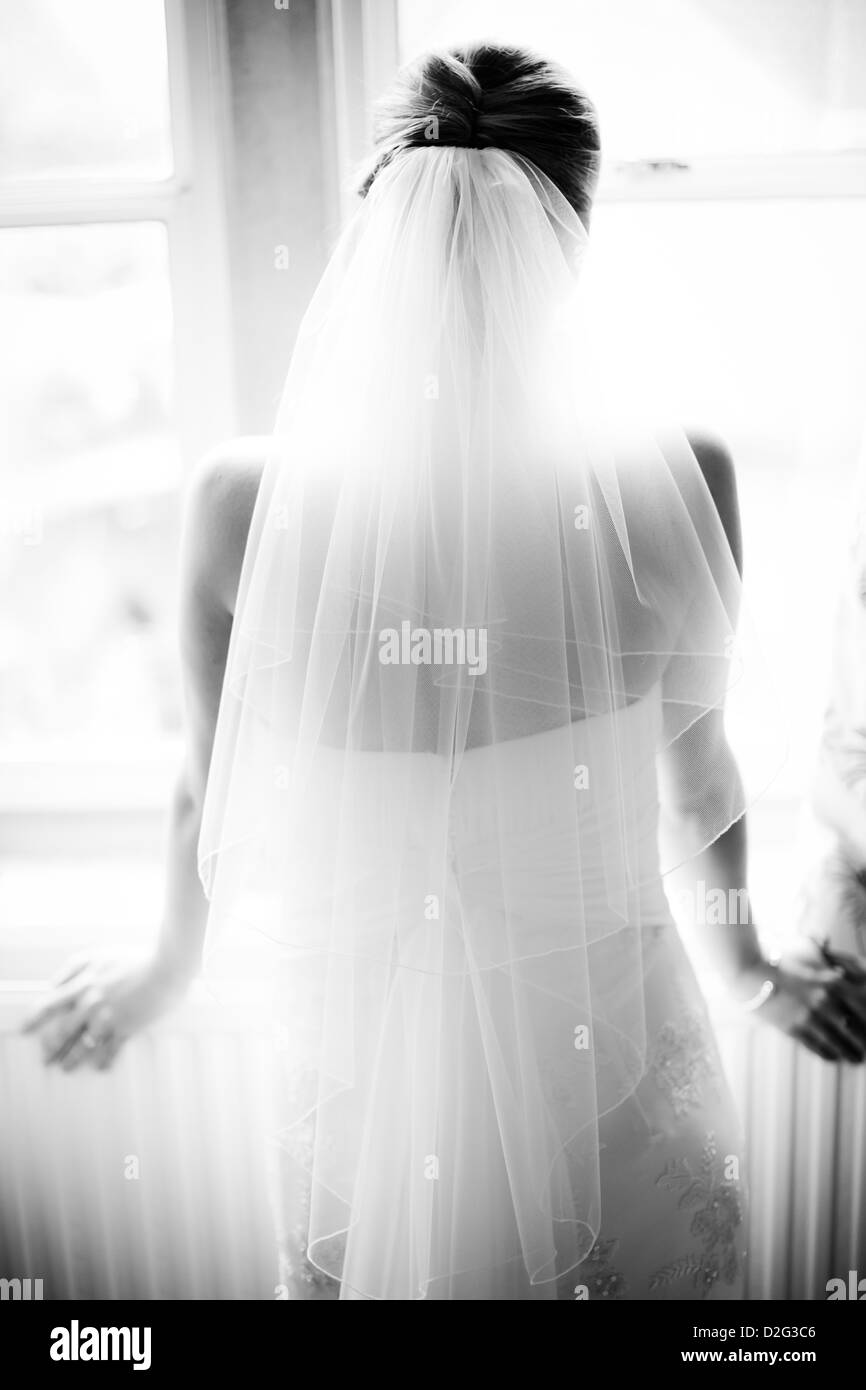 Black and white photo of a bride looking out of a window with her back and veil facing the camera Stock Photo