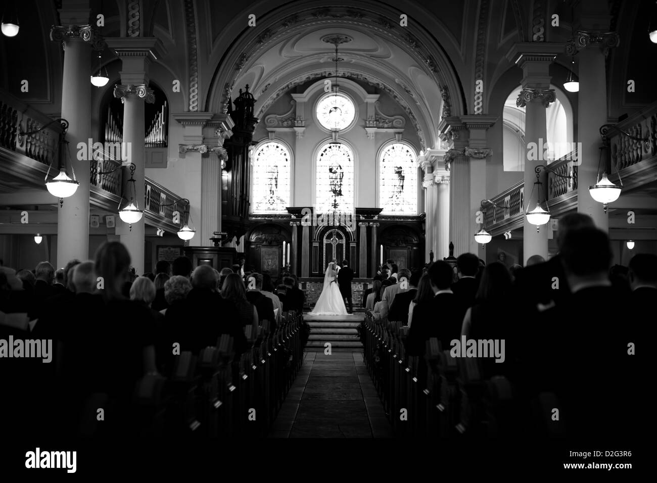 Photo of a Bride and Groom standing at the end of the aisle in a church with a full congregation. Stock Photo