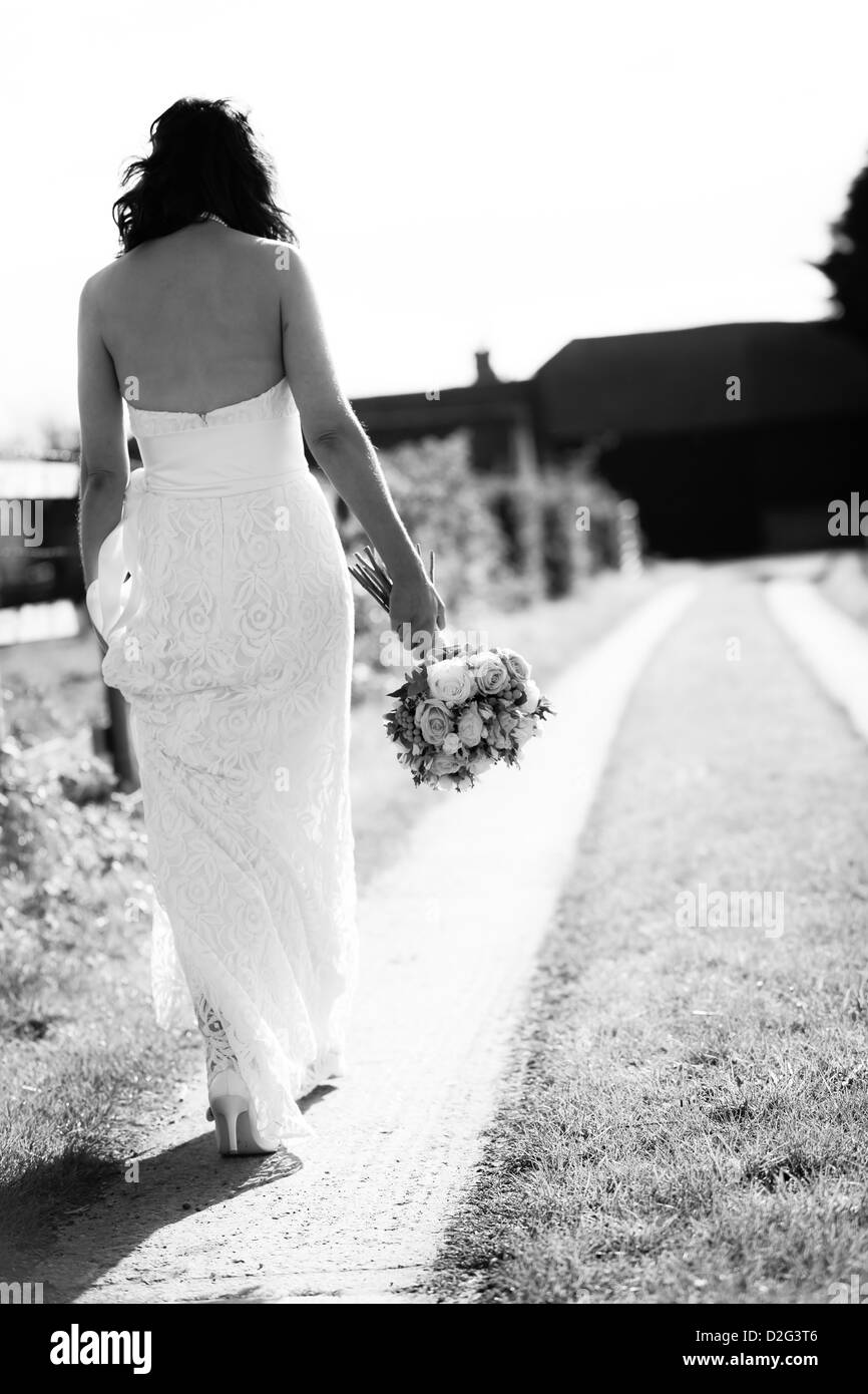A black and white photo of a bride walking outside with her bouquet in hand. Stock Photo