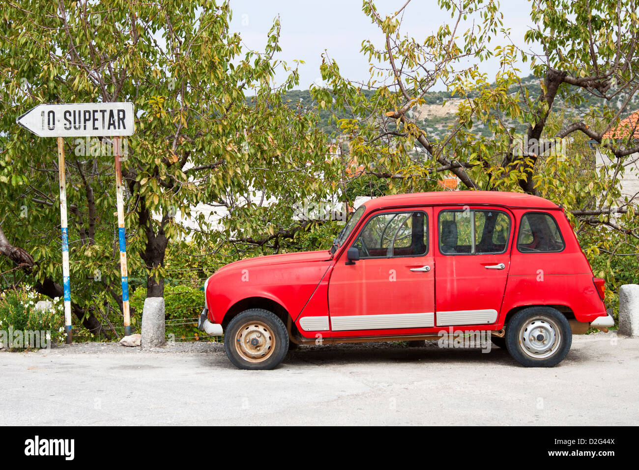An old red Renault car parked on the side of the road, next to a sign pointing to the direction of Supetar on the island of Brac Stock Photo