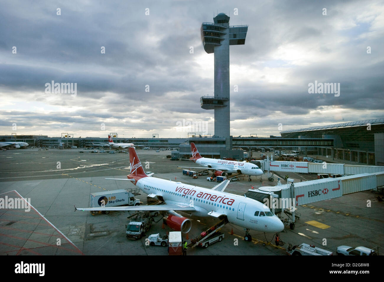 Two Virgin America Airbus A320 jet Aircraft stand in front of the Control Tower at John F. Kennedy Airport, JFK Airport, New York, USA at dusk as they are loaded for their next flights. Stock Photo