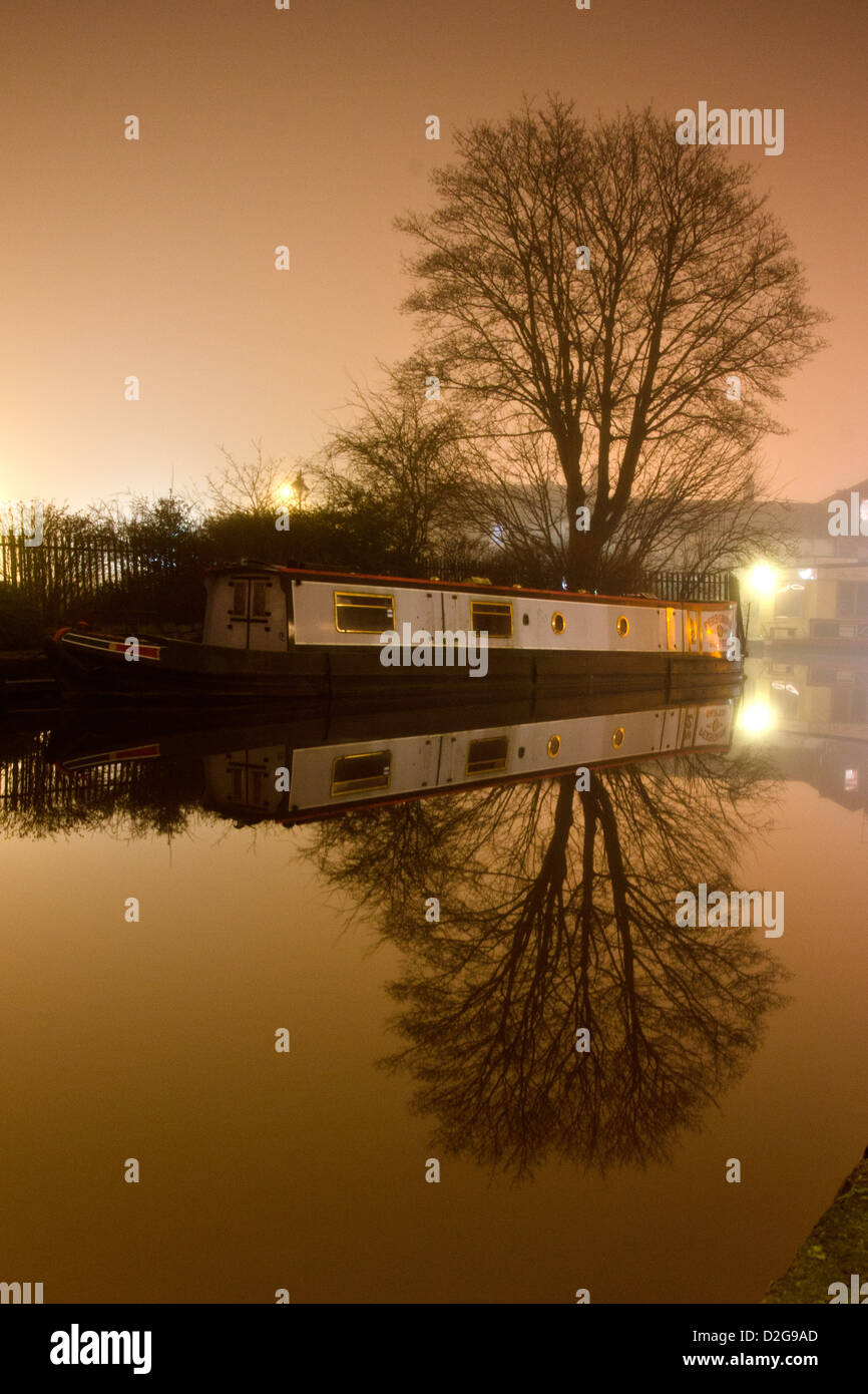Calm misty evening with a boat and a tree reflected in the water Stock Photo
