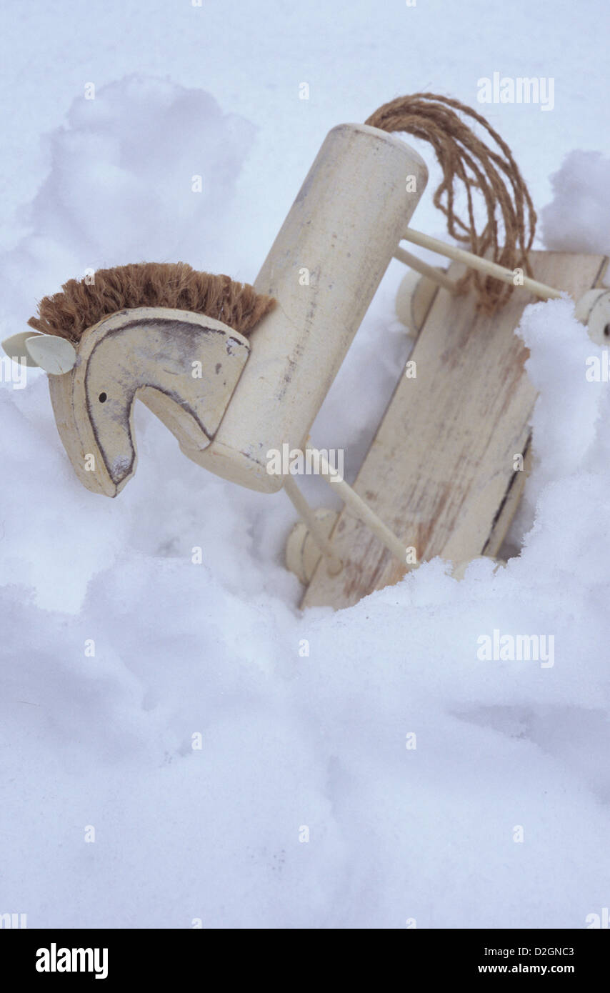 Wooden toy model of horse on wheelbase painted in stressed white and with string mane and tail sunk in soft snow Stock Photo