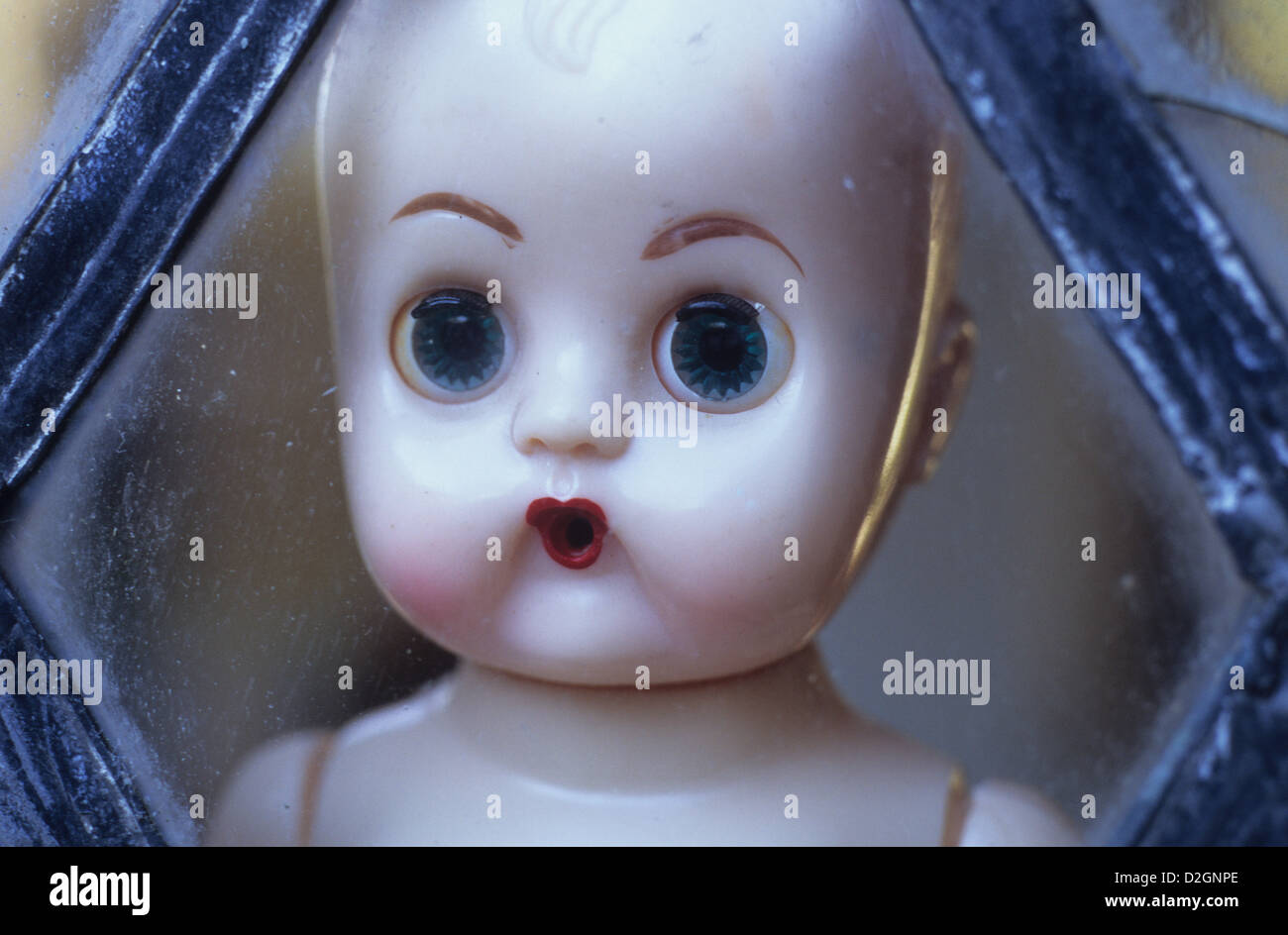 Head of traditional baby doll with big blue eyes and open mouth staring at viewer thru diamond-leaded window Stock Photo