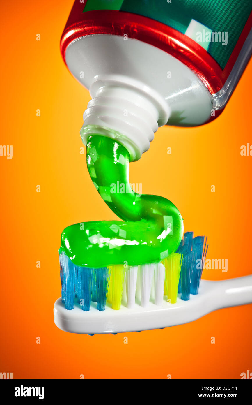 toothpaste being squeezed onto a toothbrush on a orange background