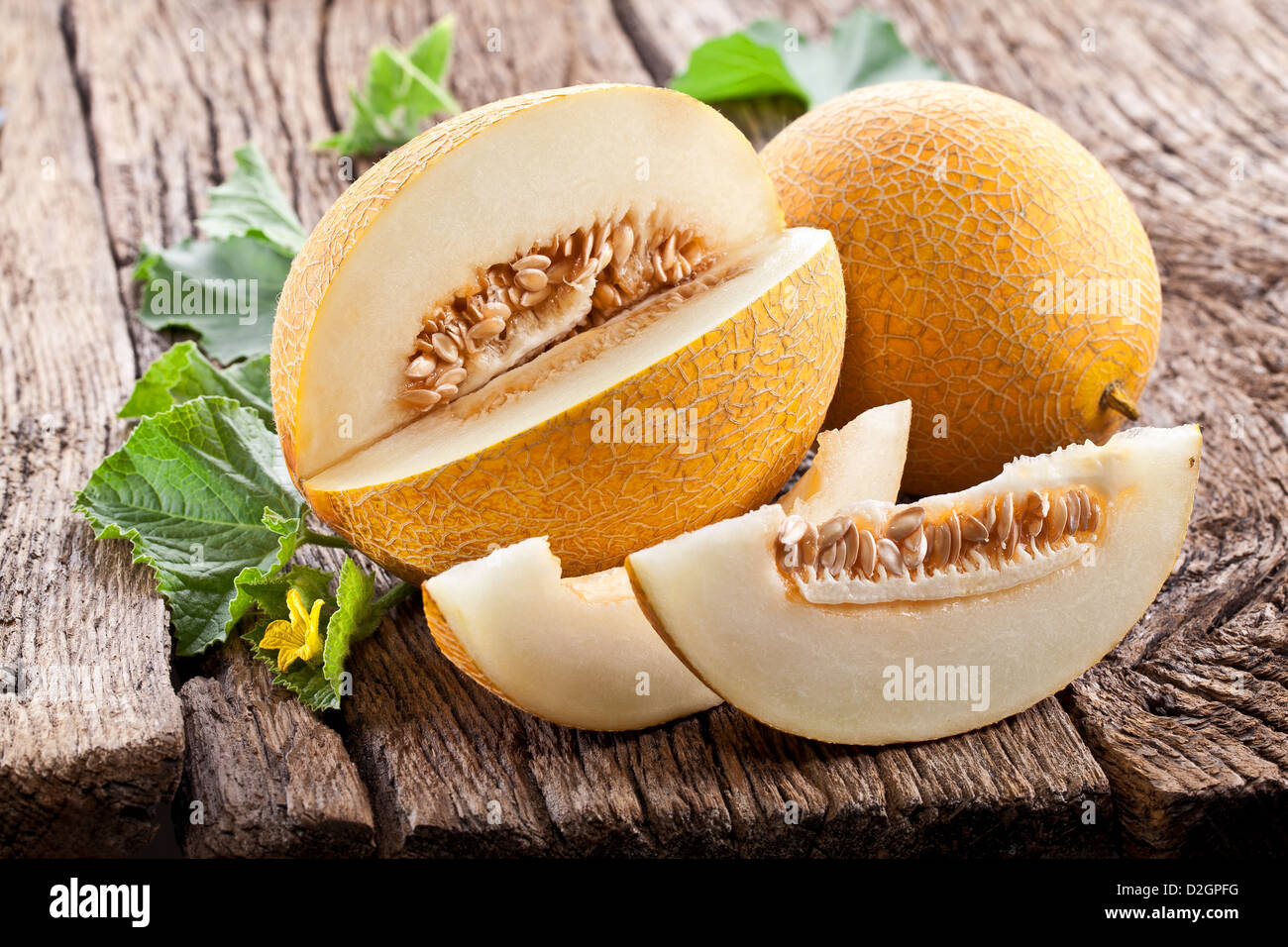 Melon with slices and leaves on a old wooden table. Stock Photo