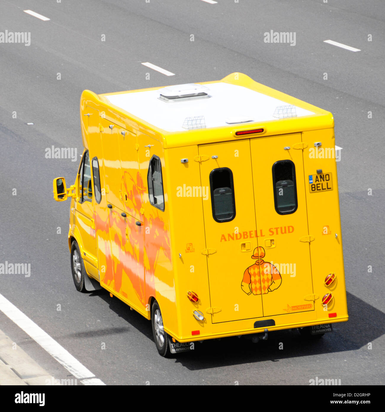 Aerial side back & rear view Andbell Stud bright yellow horsebox vehicle with personalised number plate driving along M25 motorway Essex England UK Stock Photo