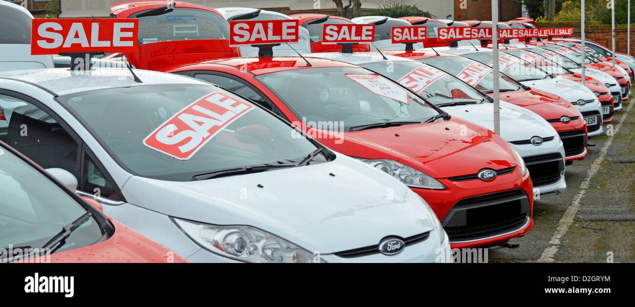 Car sale sign on used second hand Ford cars dealership pavement forecourt outside showroom alternate red and white obscured number plates England UK Stock Photo