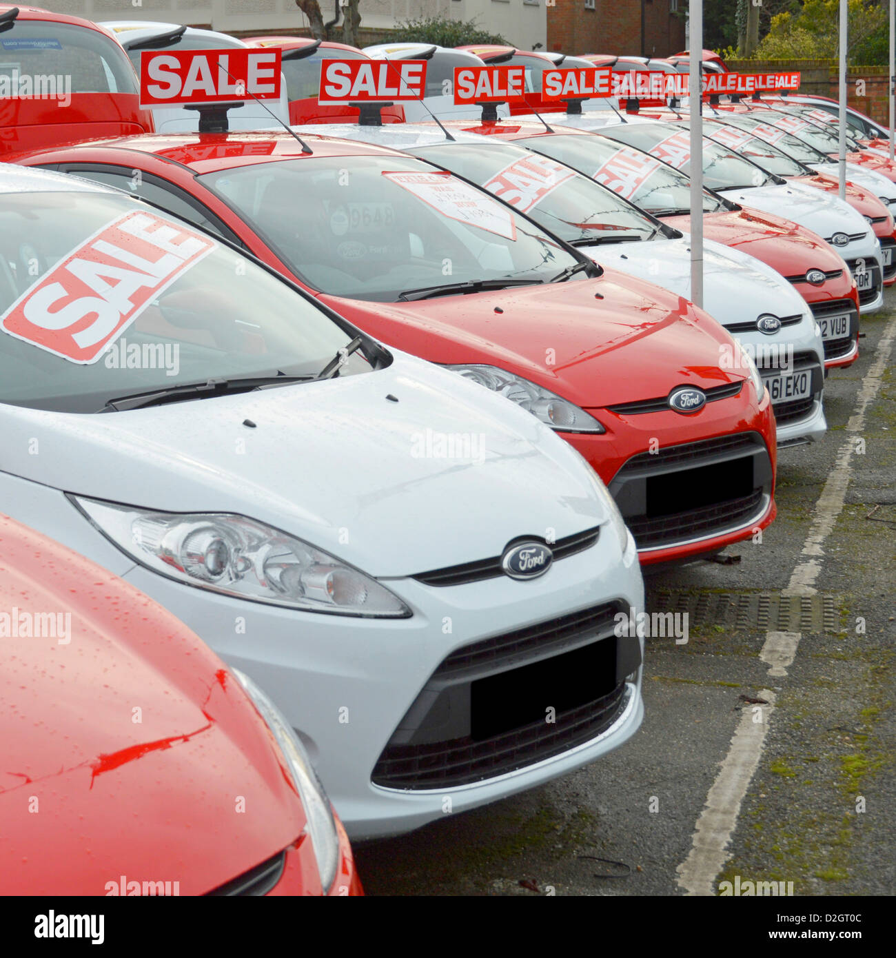 Sale of used Ford cars on car dealership pavement forecourt outside showroom arranged alternate red and white obscured number plates Essex England UK Stock Photo