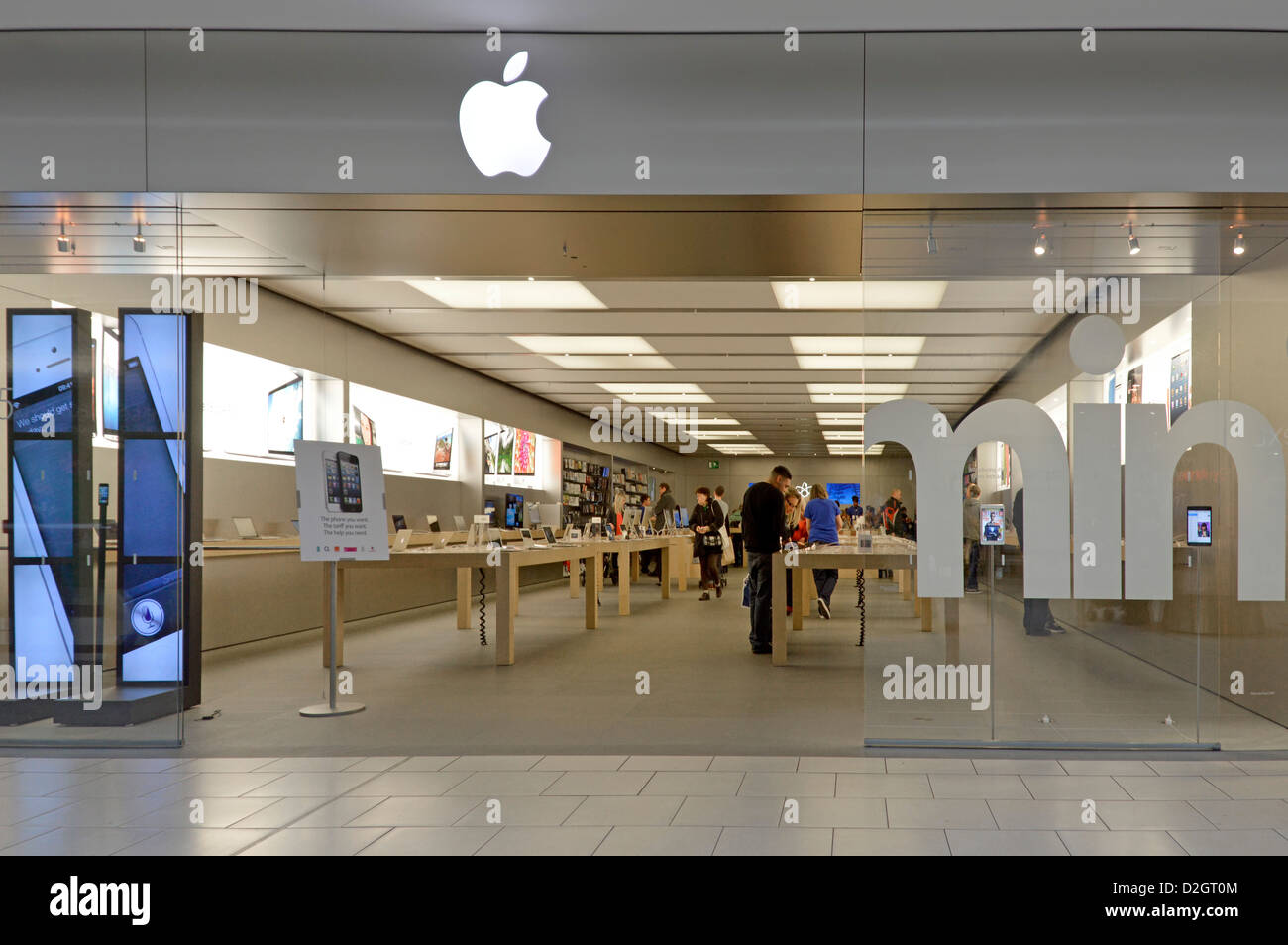 Apple logo above digital retail business computer technology store with people customers entry direct from indoor shopping mall West Thurrock Essex UK Stock Photo