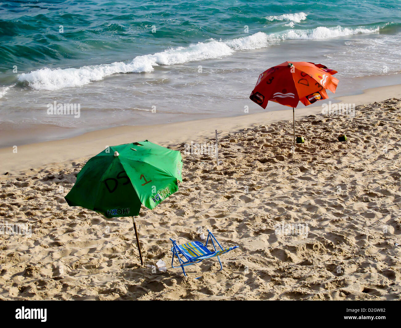 Two green and red parasols and a sun chair on a sandy  beach in Salvador, Brazil Stock Photo