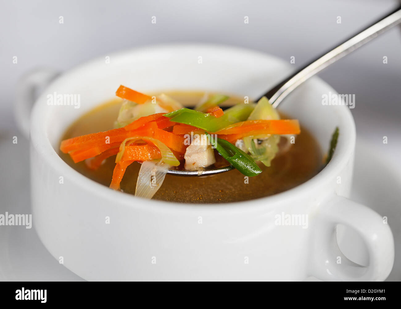 Chicken soup with vegetables in spoon and white deep plate Stock Photo