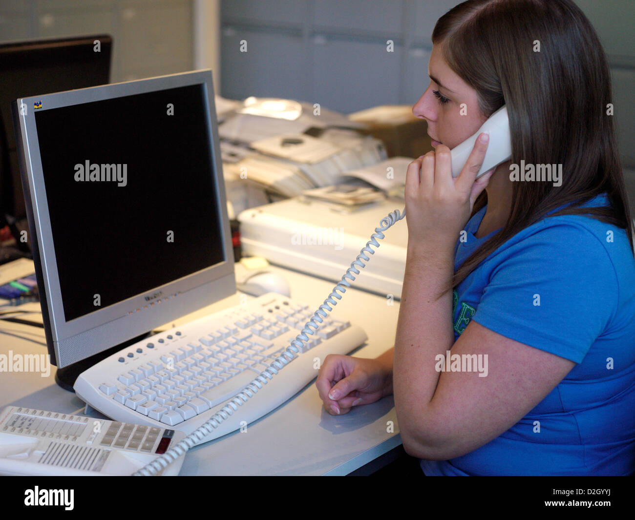 Young Woman Looking at a Blank Computer Screen and Holding a Corded Phone Stock Photo