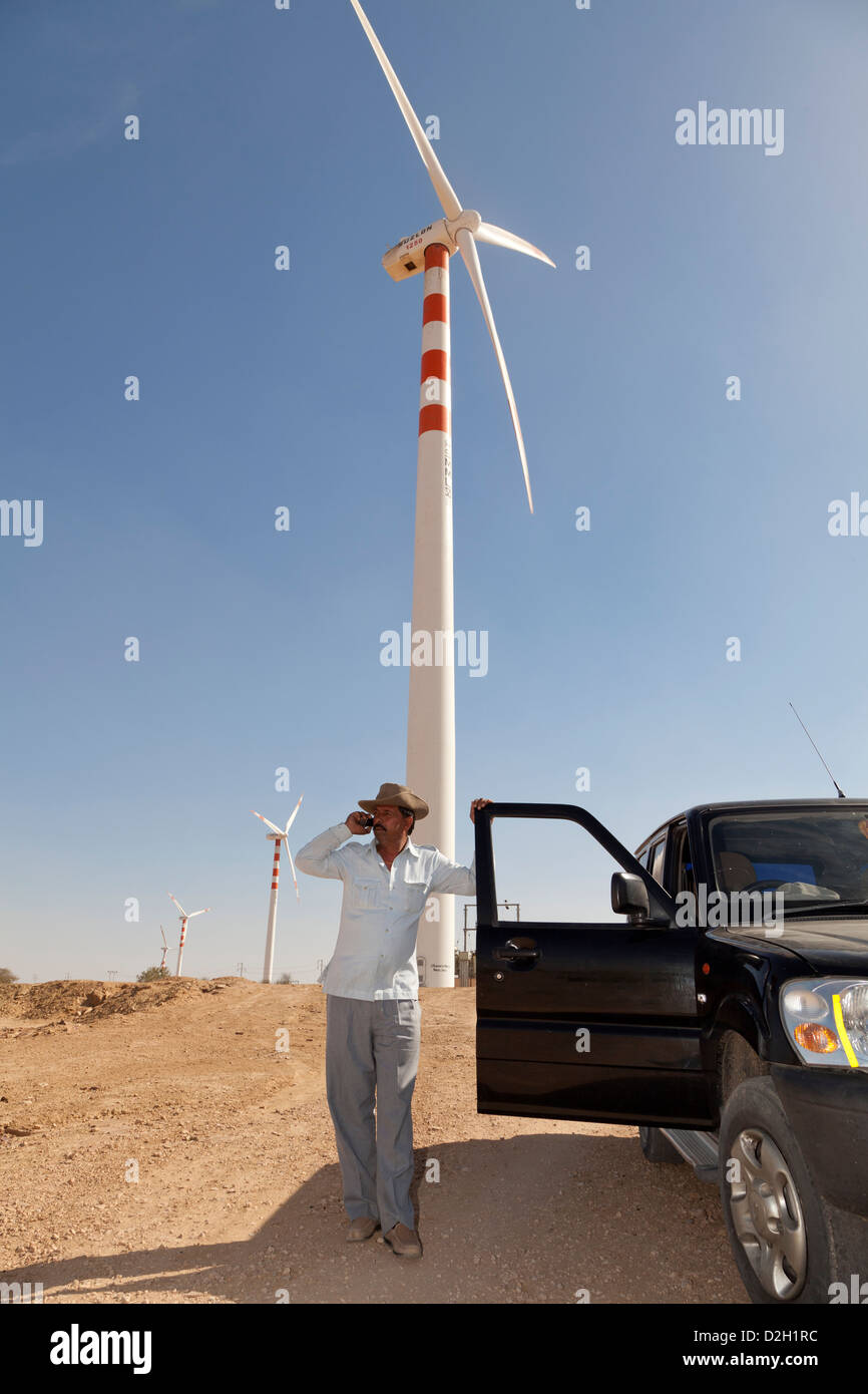 India, Rajasthan, Thar Desert, Engineer standing by wind turbines using mobile phone Stock Photo