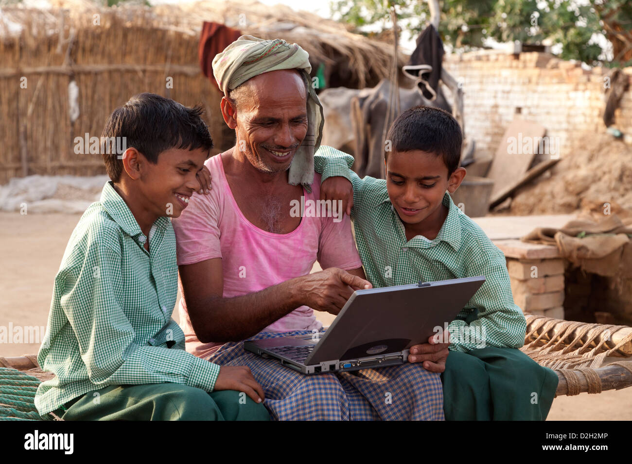 India,Uttar Pradesh, Agra, Two young children in school uniform studying laptop with father. Stock Photo