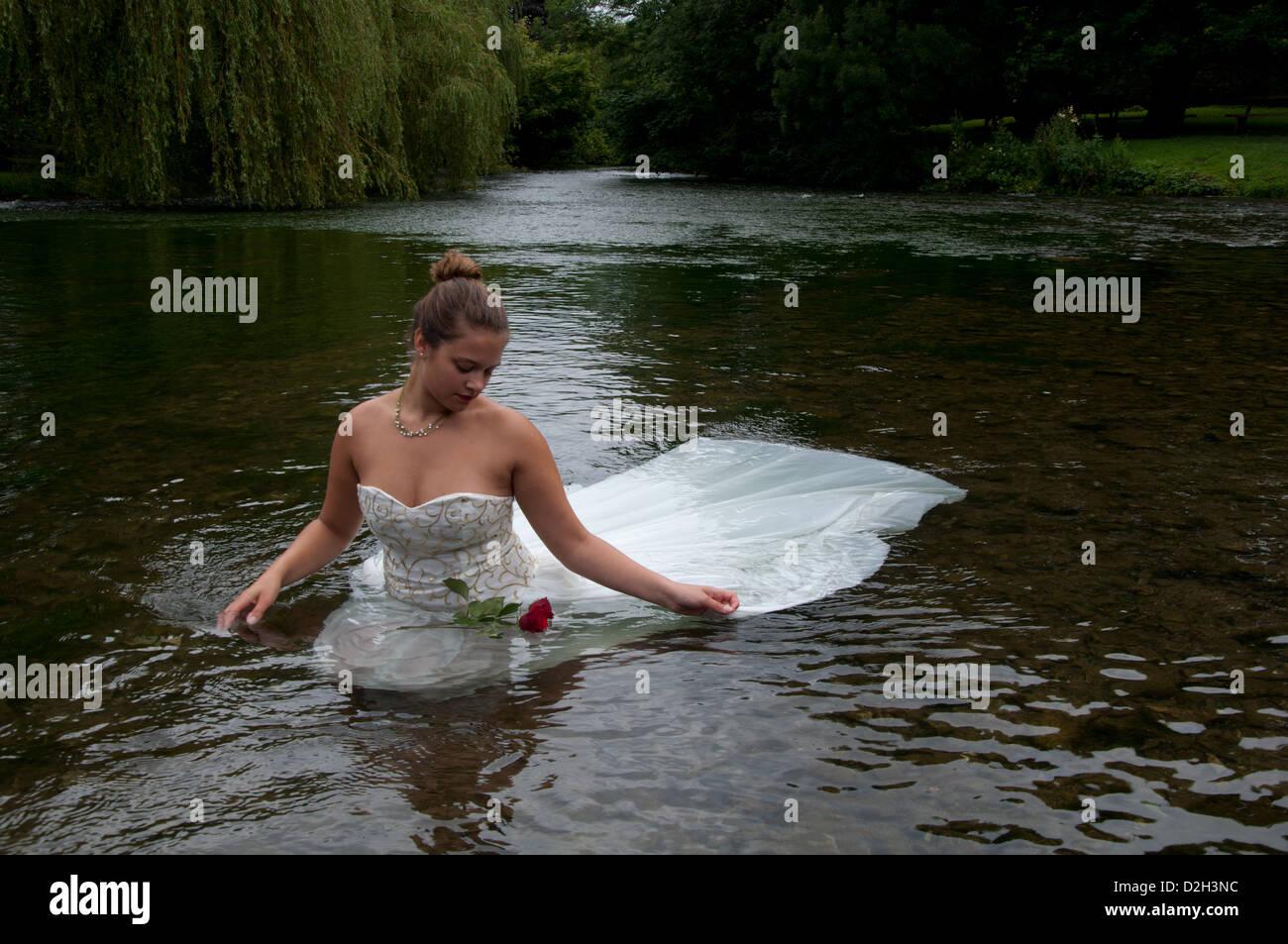 Young lady in a white wedding dress in a river watching roses floating ...