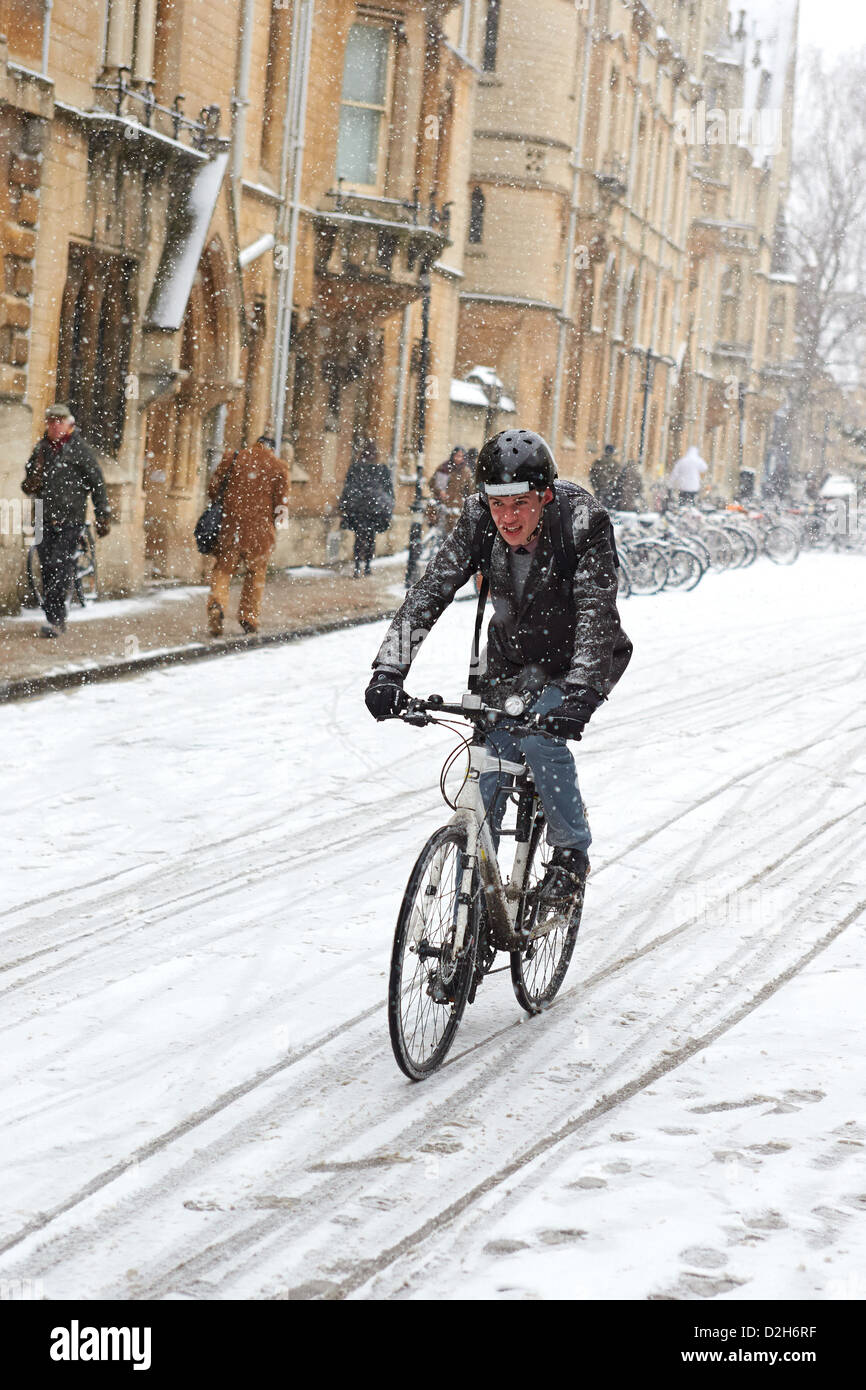 A student cycles through central Oxford during heavy snow Stock Photo