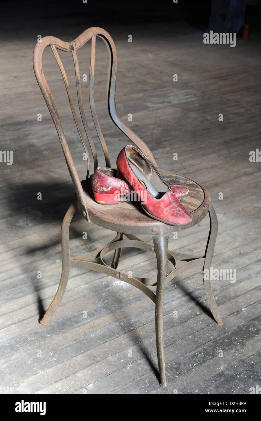 Old red worn out shoes on rusty metal chair with dirty wooden floor for a background. Stock Photo