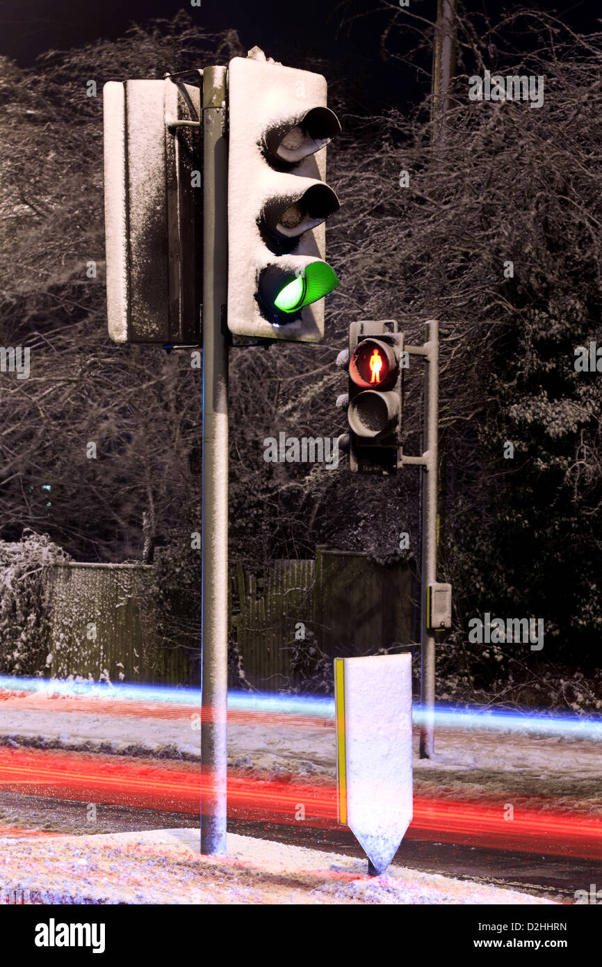 Traffic lights covered in snow on a UK road at night with light trails from passing cars. Stock Photo