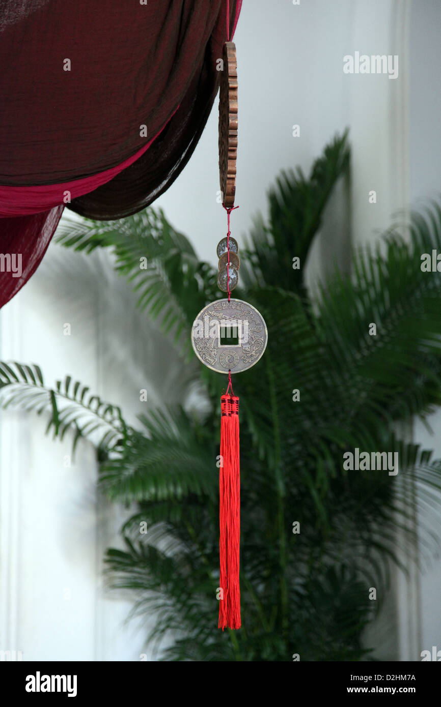 It's a photo of a medallion or a Chinese coin suspended or attached go a red rope.. We can see a red Curtain and a green plants Stock Photo