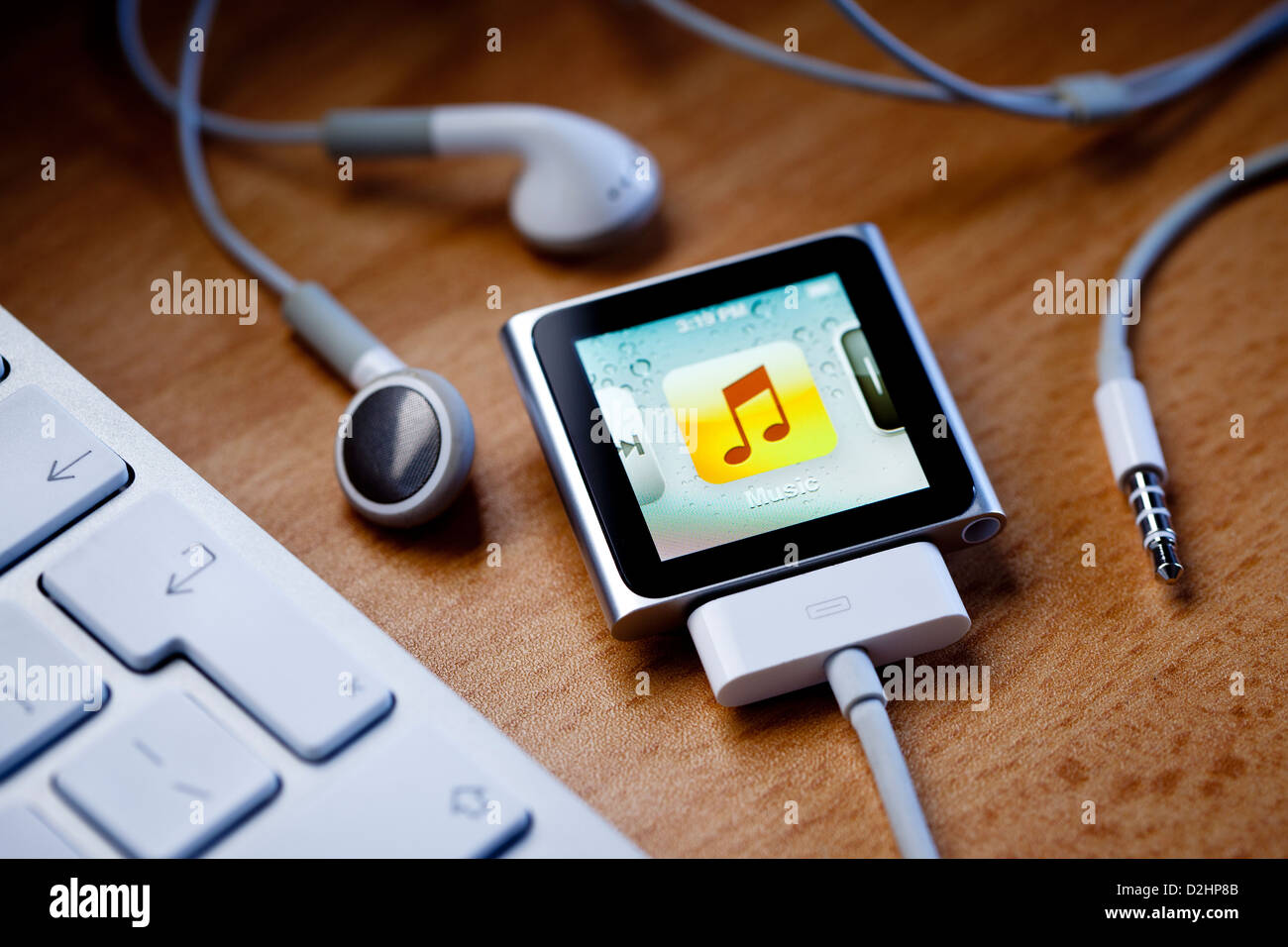 iPod Nano with a cable attached, sits on a desk next to Apple earbud headphones and a computer keyboard. Stock Photo