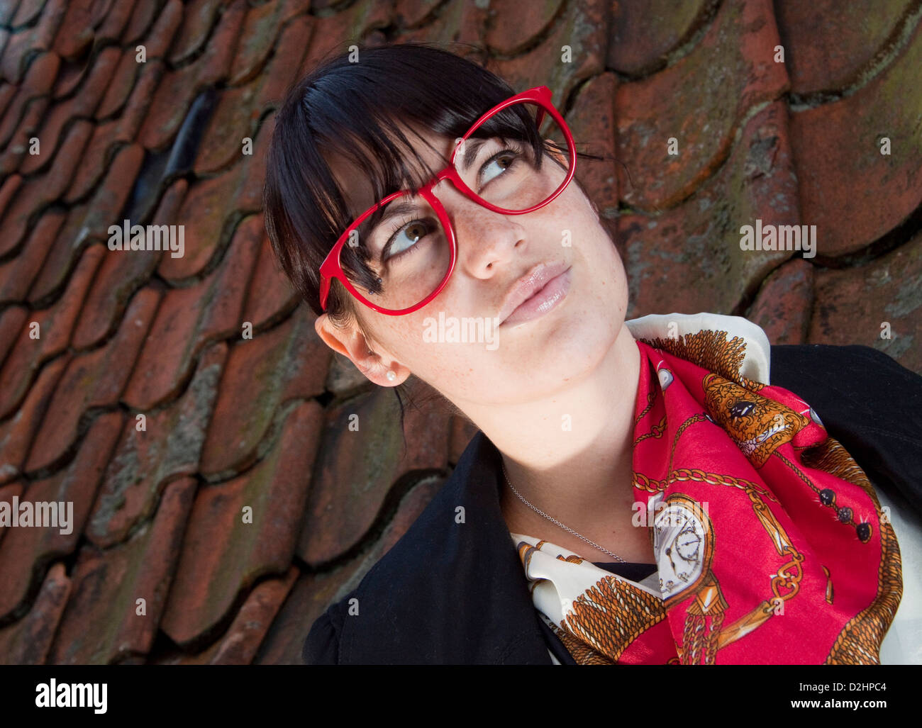 Portrait of attractive dark haired young woman in big glasses against red tile background Stock Photo