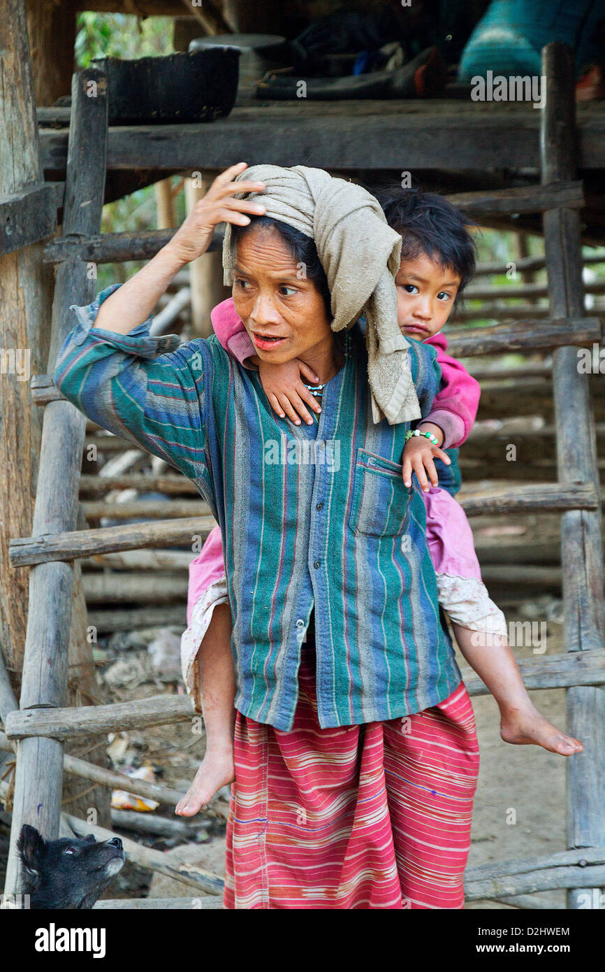 A mother carrying her daughter on one's back in the entrance of a simple house, village in the mountains. Chiang Mai Province. Stock Photo