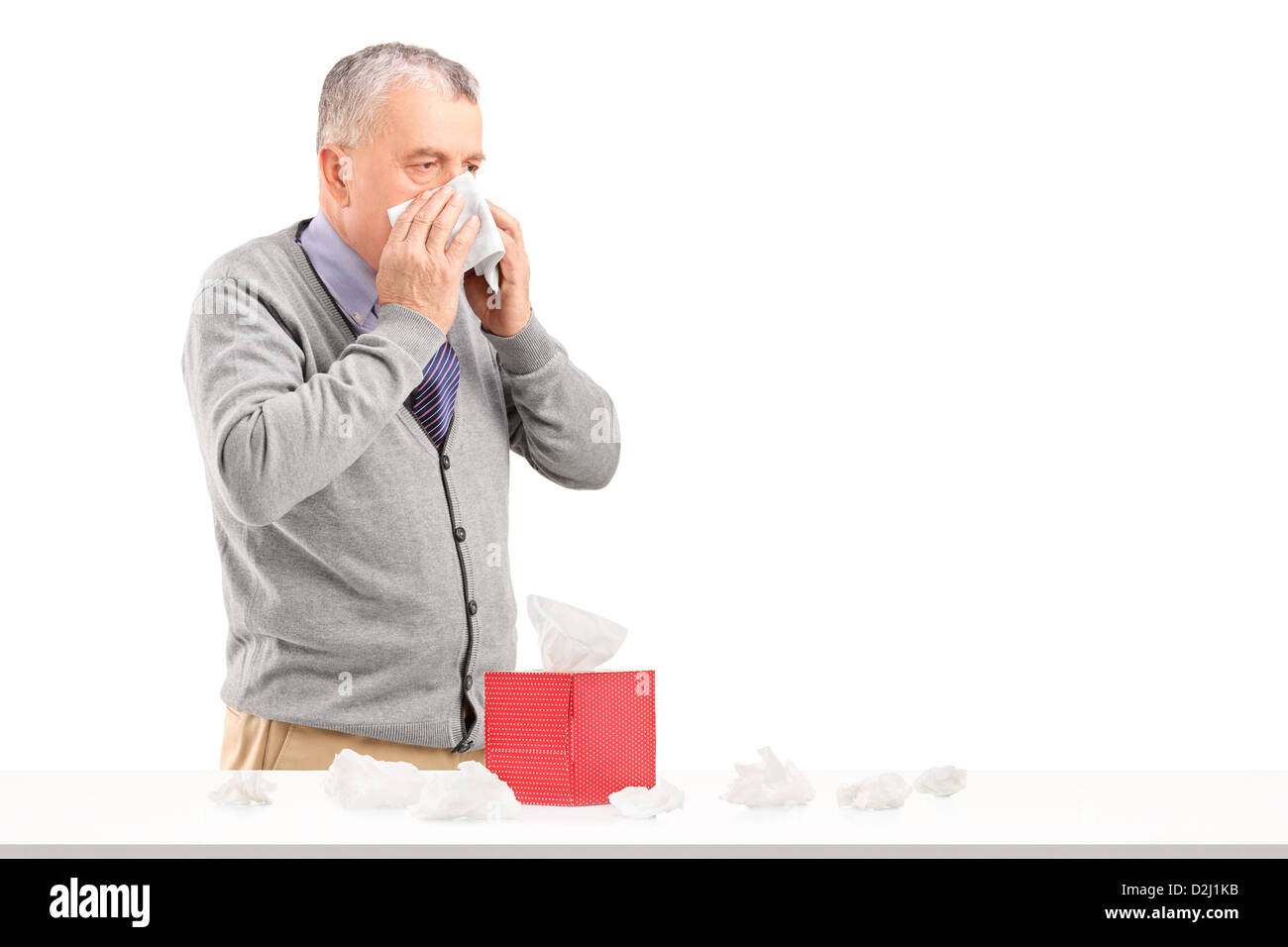 Man blowing nose with a box of tissues on a table isolated on white background Stock Photo