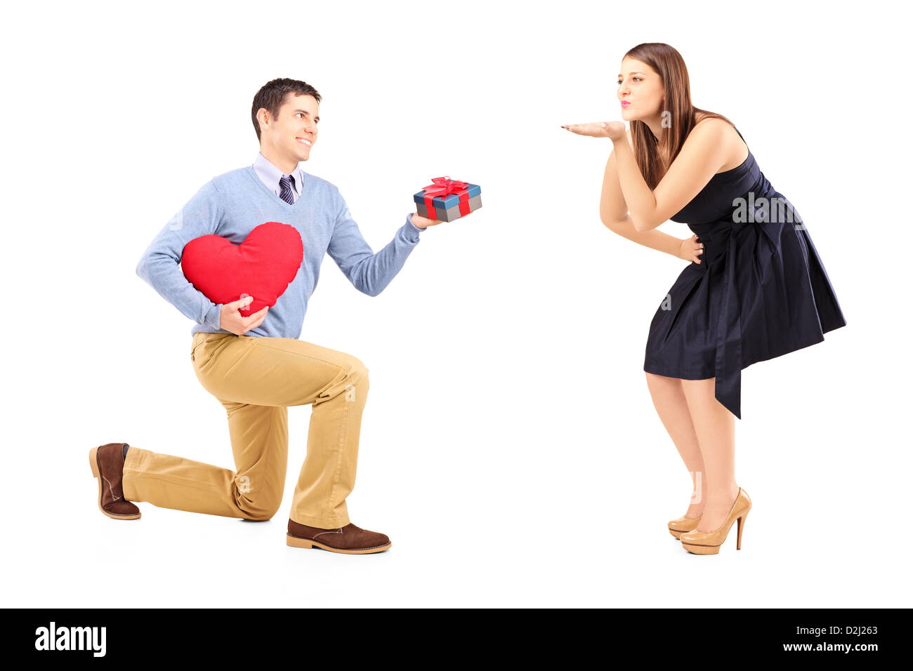 Smiling male on kneel with a red heart giving and a present to a woman blowing him a kiss isolated on white background Stock Photo