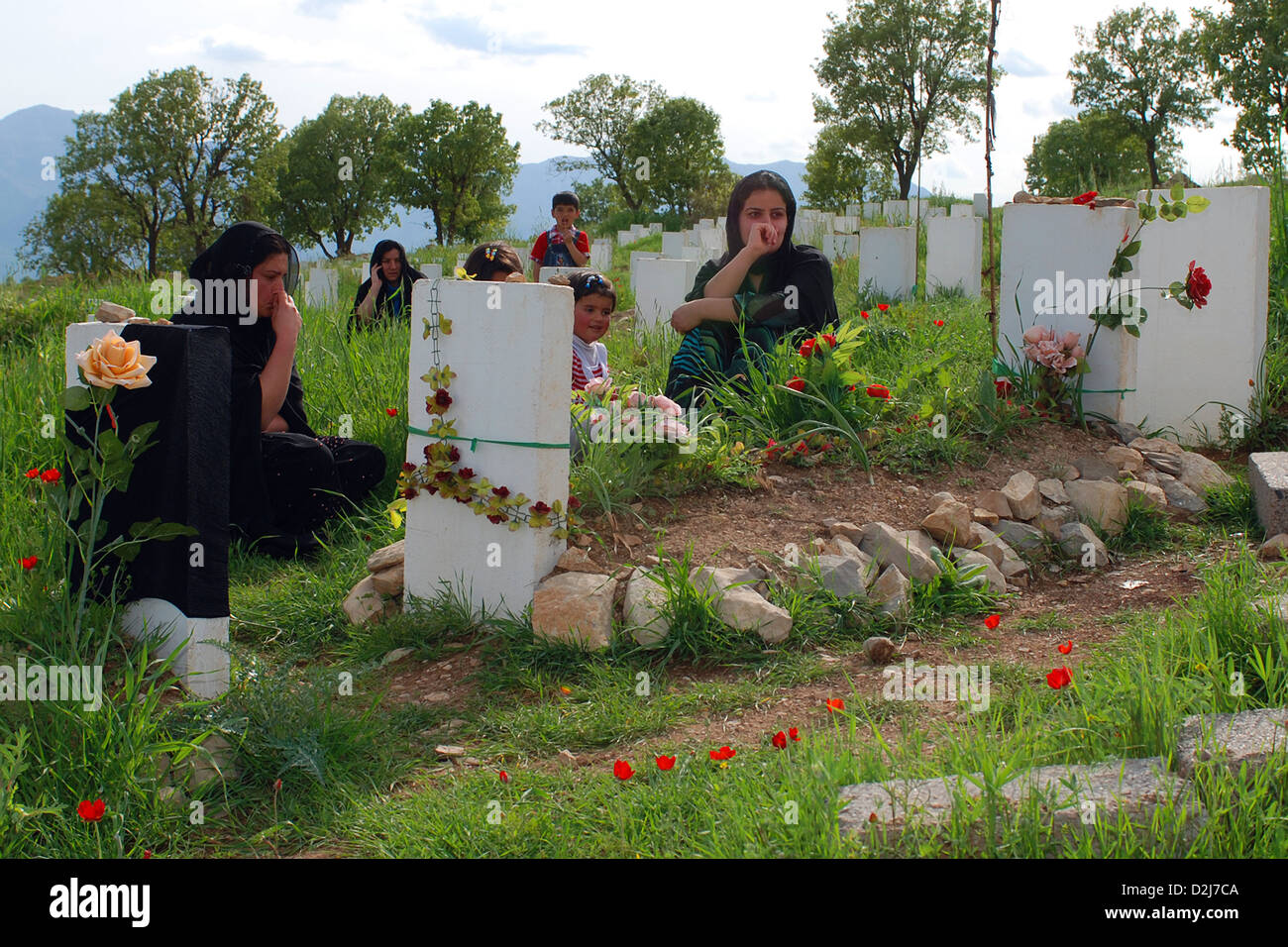 Kurdish women and children visit the grave site of a loved one in a cemetery where approximately 500 Kurdish men and boys who were killed during the early years of Saddam Hussein's regime have been relocated. The remains were brought from the mass burial site near Bussia, Iraq, and given a proper burial where they are now in Barzan, Iraq. Stock Photo