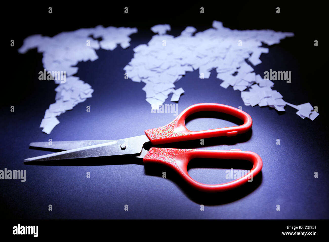 Red scissors in front of world map made of small papers. Stock Photo