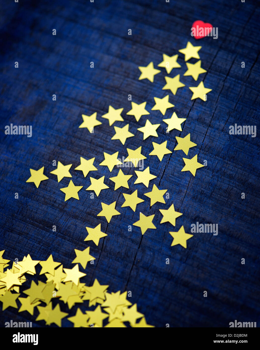 Shiny gold stars and red heart in the shape of a Christmas tree on a dark blue wood background Stock Photo