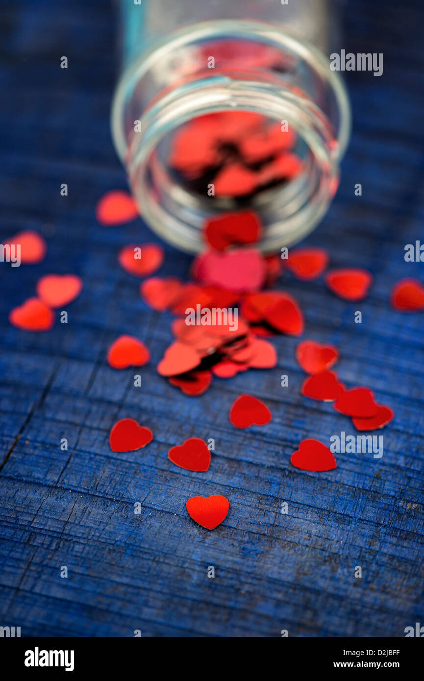 Shiny red love hearts coming out of a glass jar on blue wood background Stock Photo