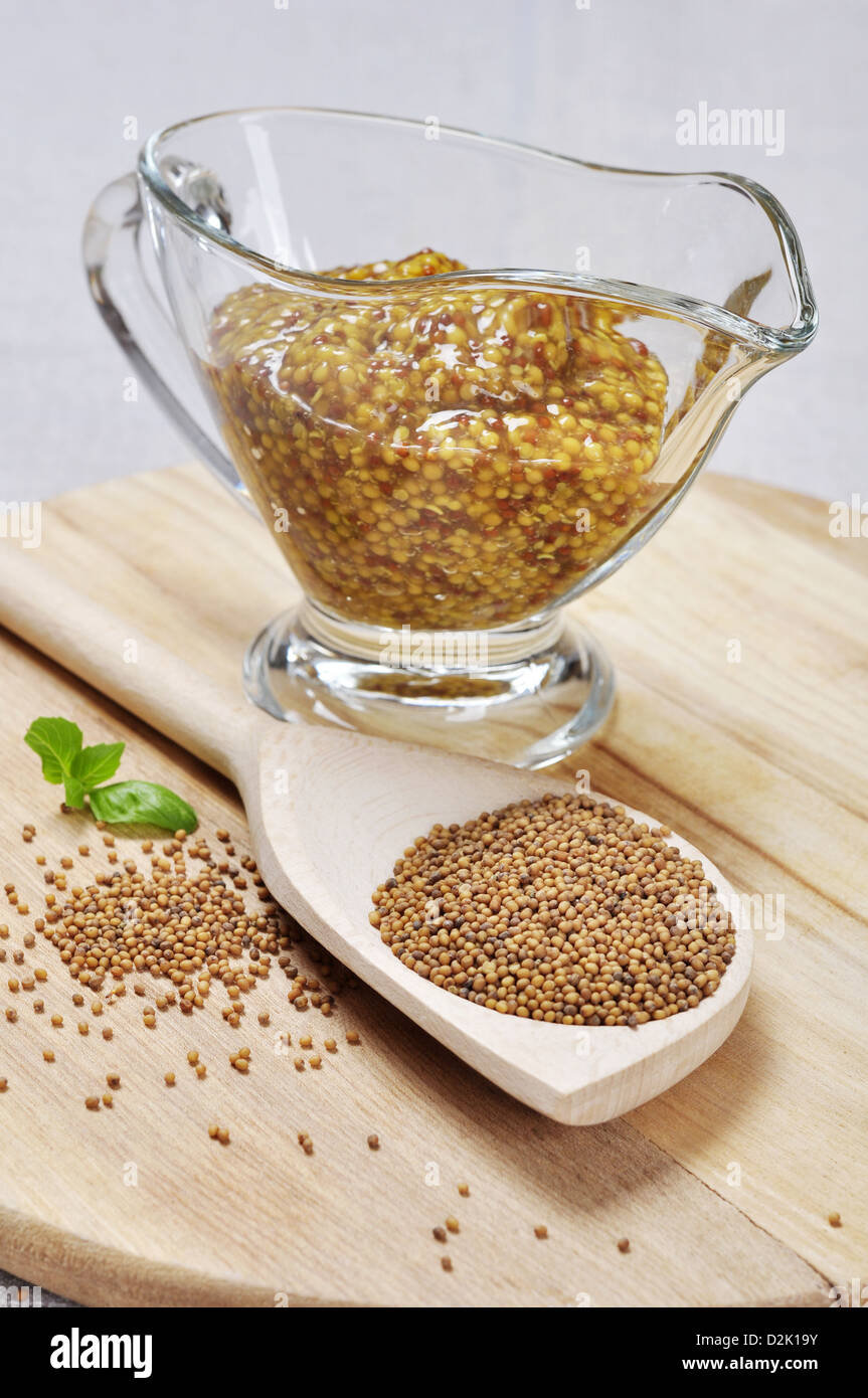 Mustard sauce in a gravy boat and mustard seeds in a wooden spoon Stock Photo