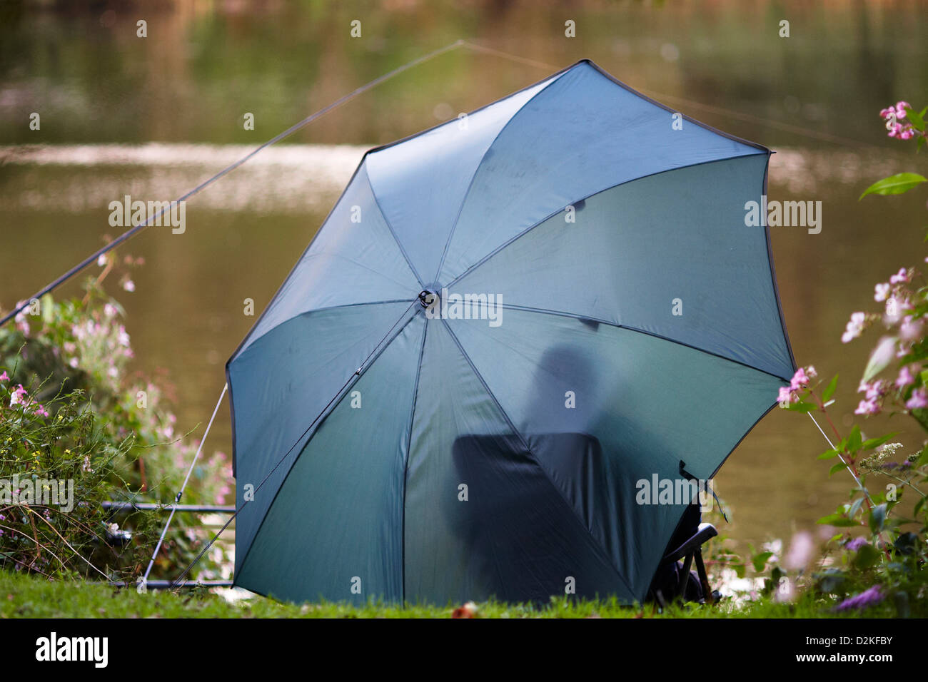 Person fishing, sitting and relaxed under an umbrella to protect from