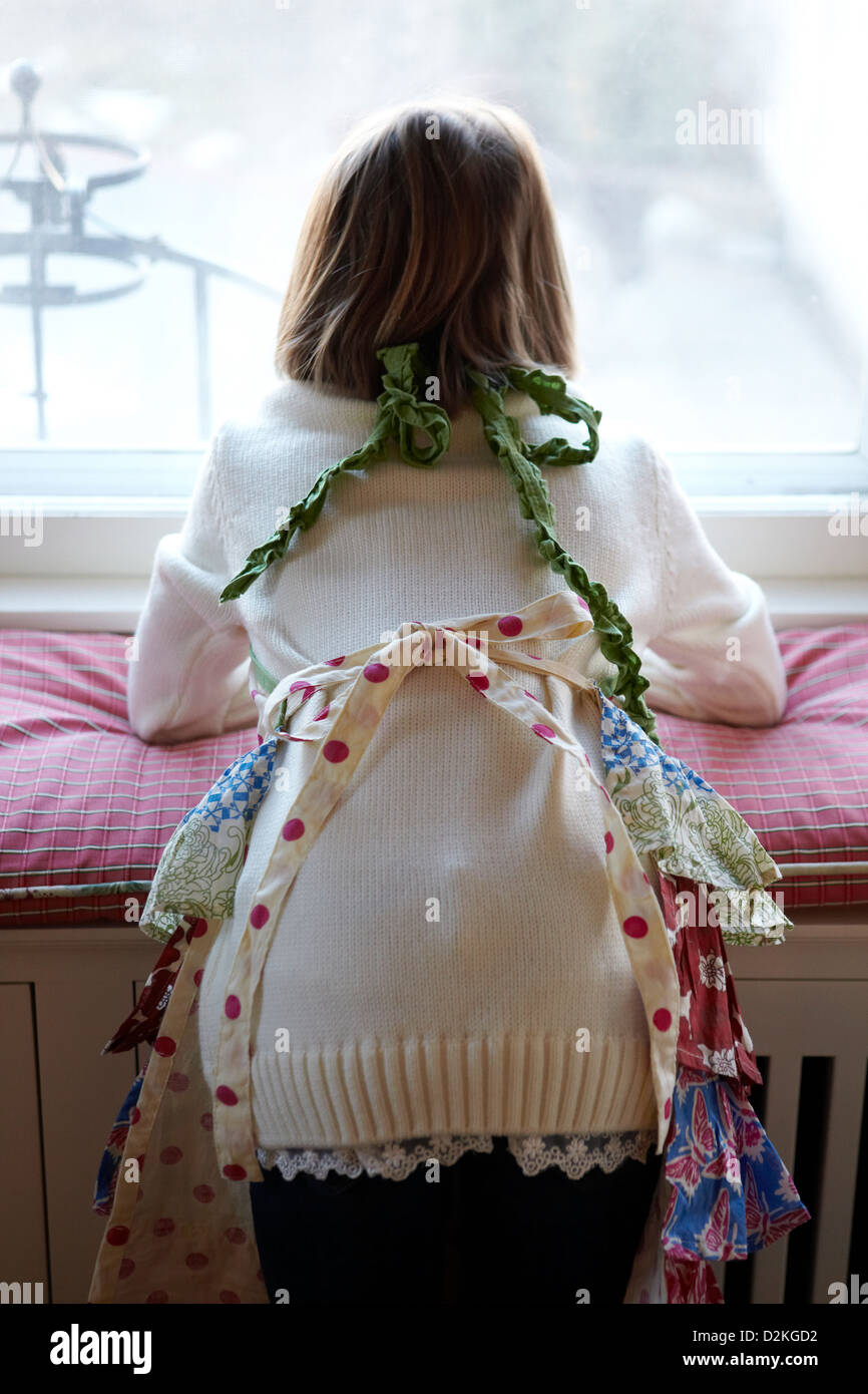 Child wearing apron looking out window from behind Stock Photo