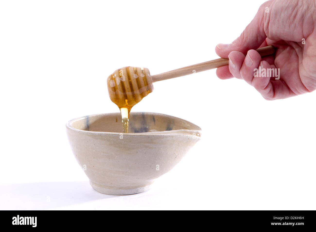 Man's hand holding a dripping honey dipper over a bowl. Stock Photo