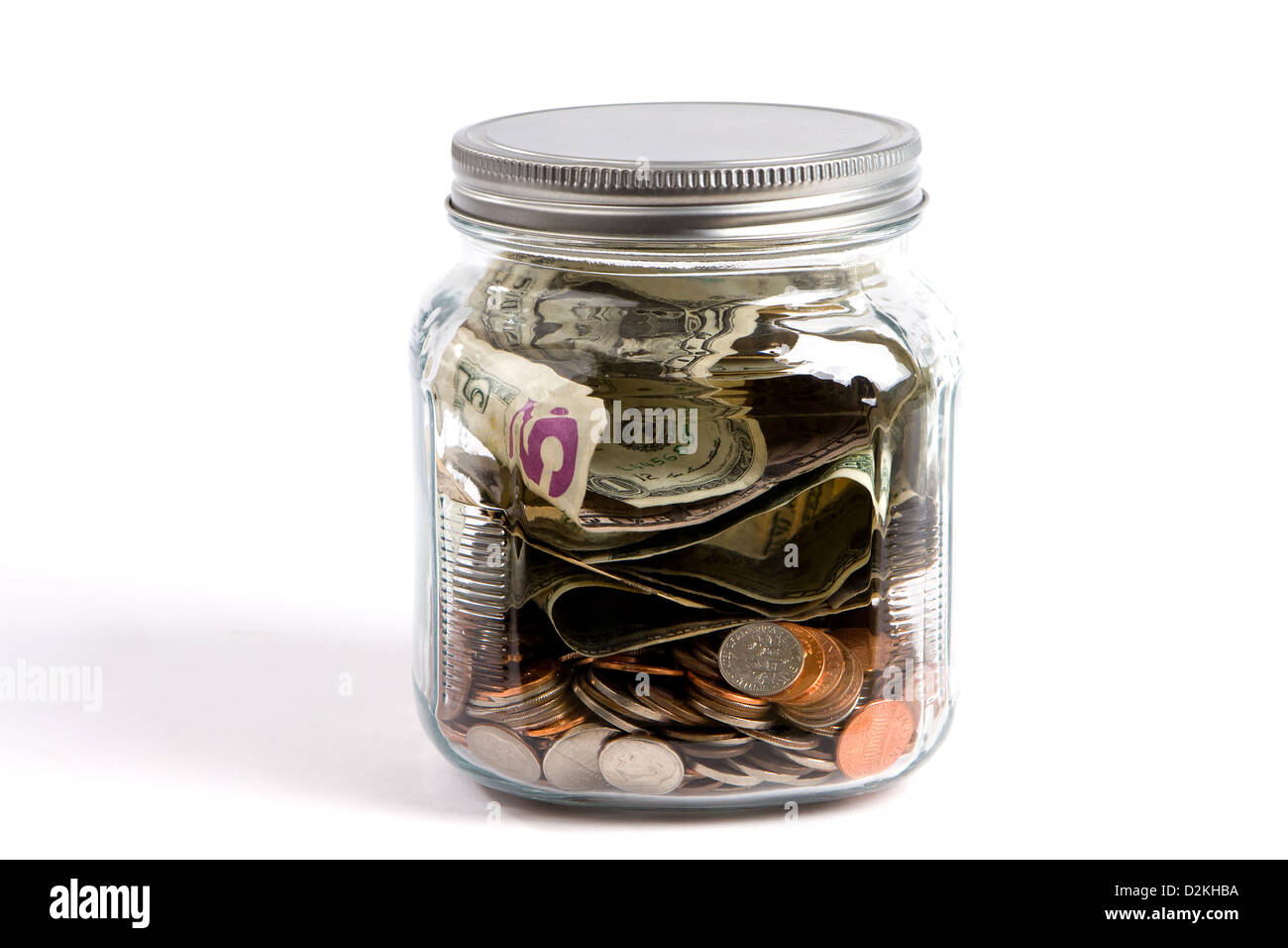 Clear glass jar filled with USA dollars and coins sit on a white background financial concept. Stock Photo