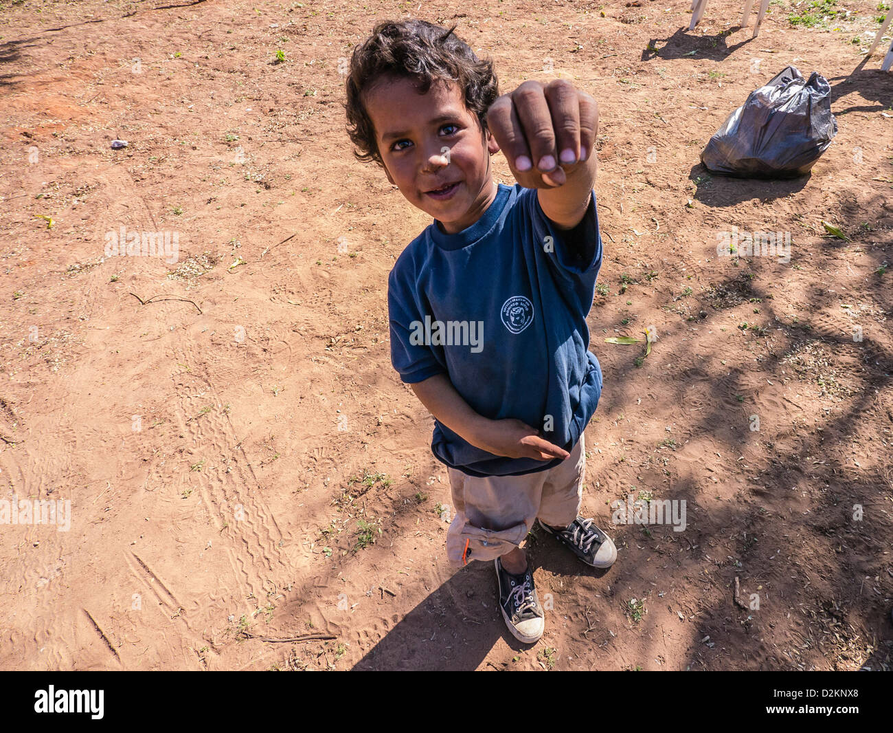 A view, looking down on a young boy in Paraguay holding his hand up and smiling. He wears a t-shirt and smiles. Stock Photo