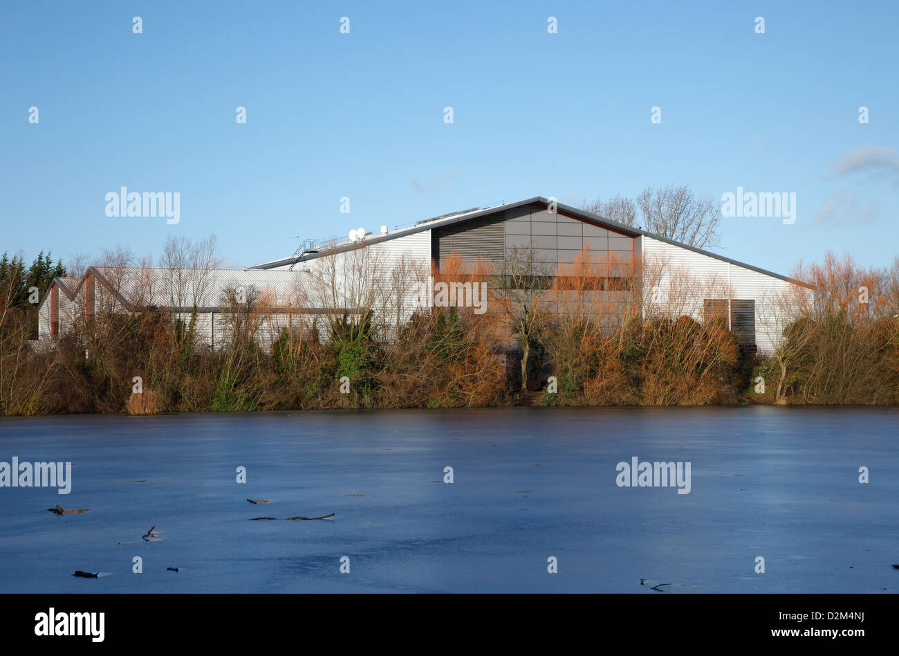 Industrial building overlooking lake in winter with ice on lake Milton Cambridgeshire Stock Photo