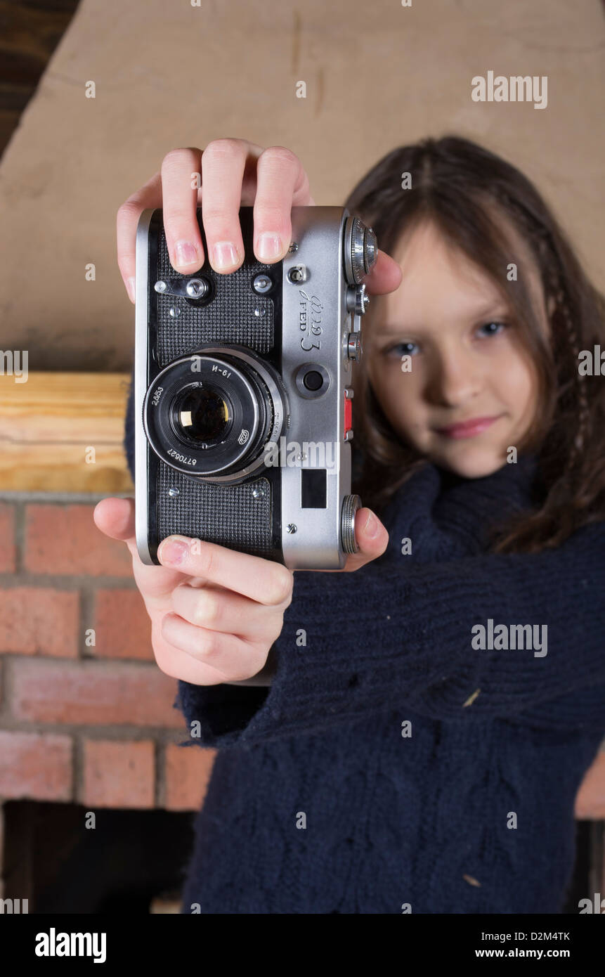 young girl in blue jersey with vintage photo camera near red brick fireplace Stock Photo