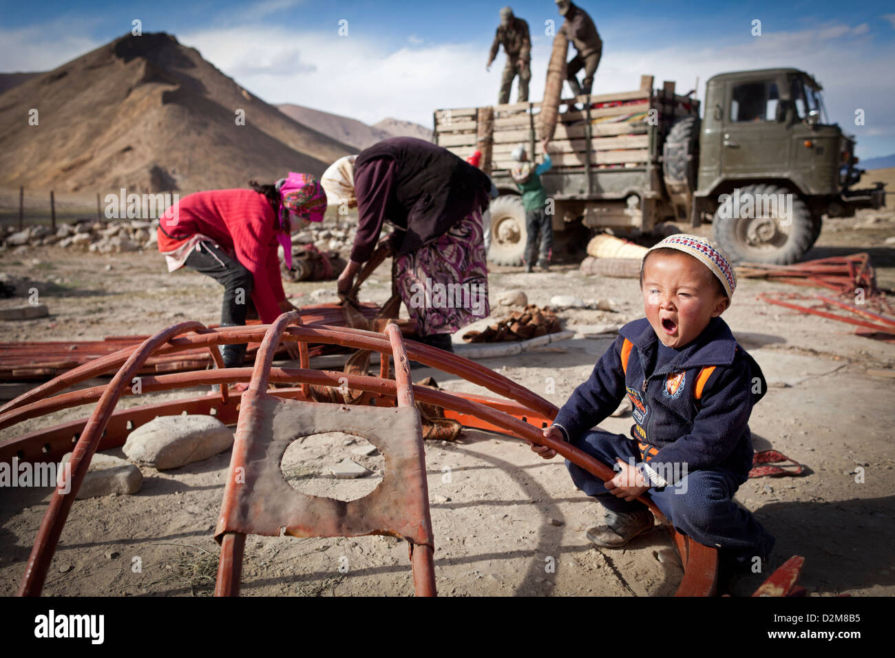 A Kyrgyz boy yawns while his family takes down a yurt camp in eastern Tajikistan. Stock Photo