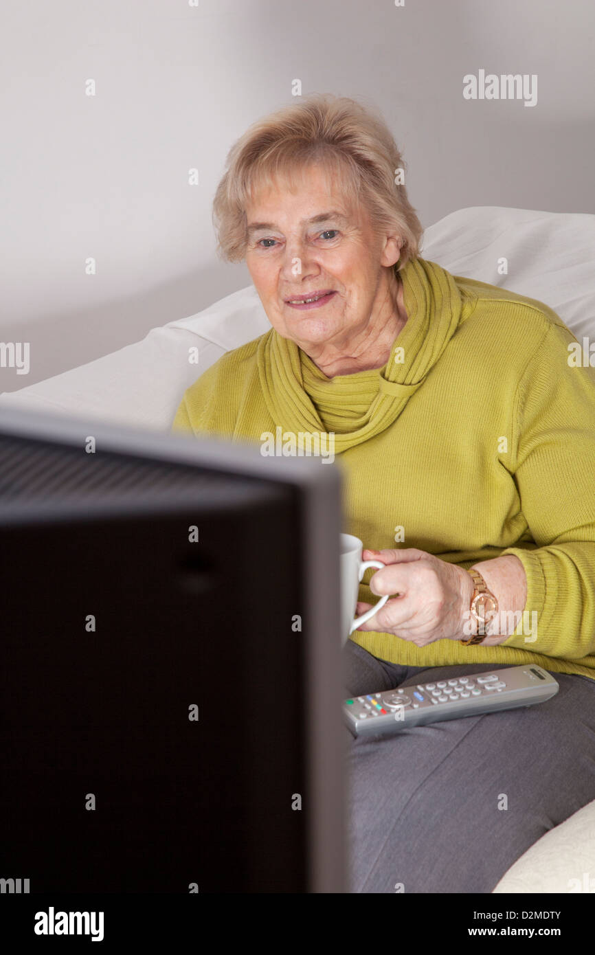 Mature lady sitting holding the a mug of tea or coffee, watching TV. Stock Photo