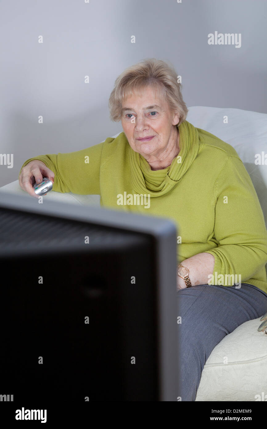 Mature lady sitting holding the remote control, watching TV. Stock Photo