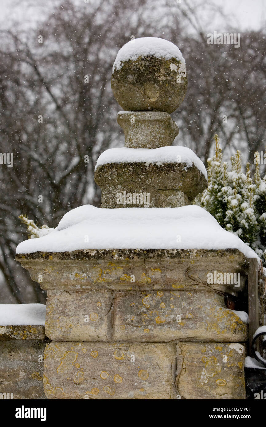 Snow falling on old stone gate post finial, masonry ball with out of focus trees in the background. Stock Photo