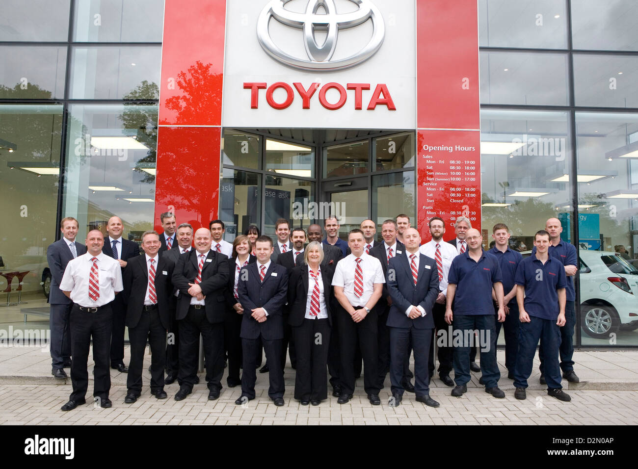 The staff of a Toyota car dealership pose for a group photo outside the entrance. Stock Photo